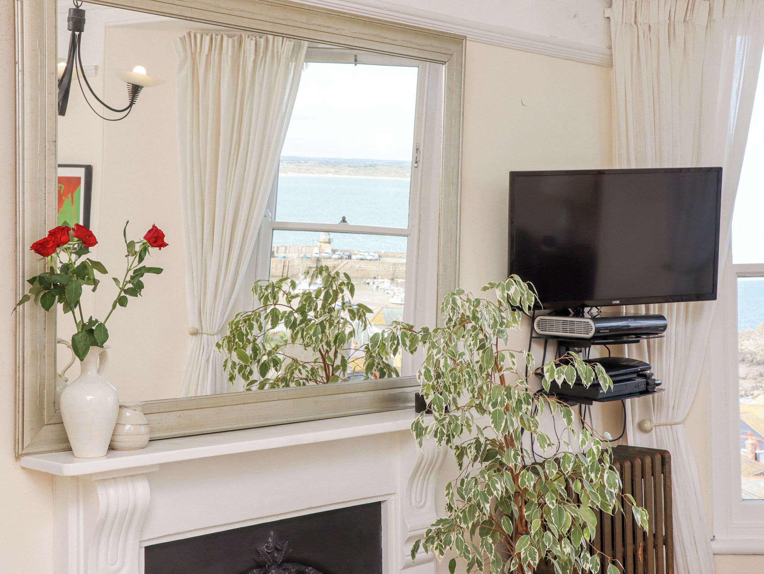A room with a fireplace, a television mounted on the wall, and a view of the sea through a window.