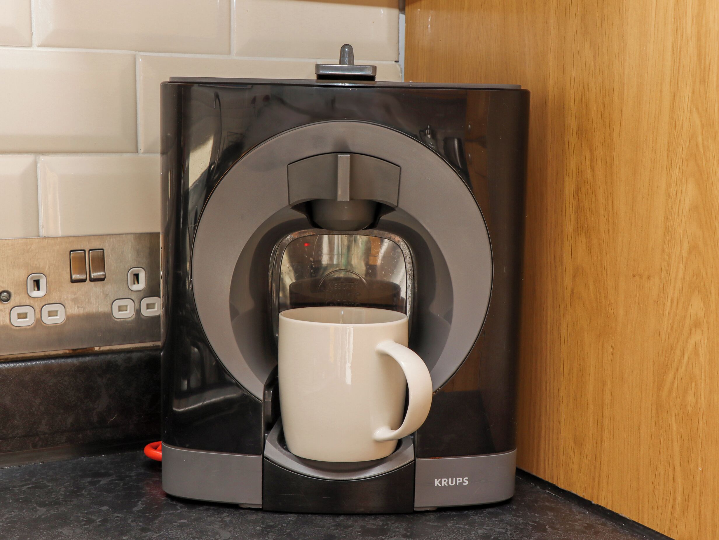 Une machine à café Krups avec une tasse blanche posée sur le comptoir.