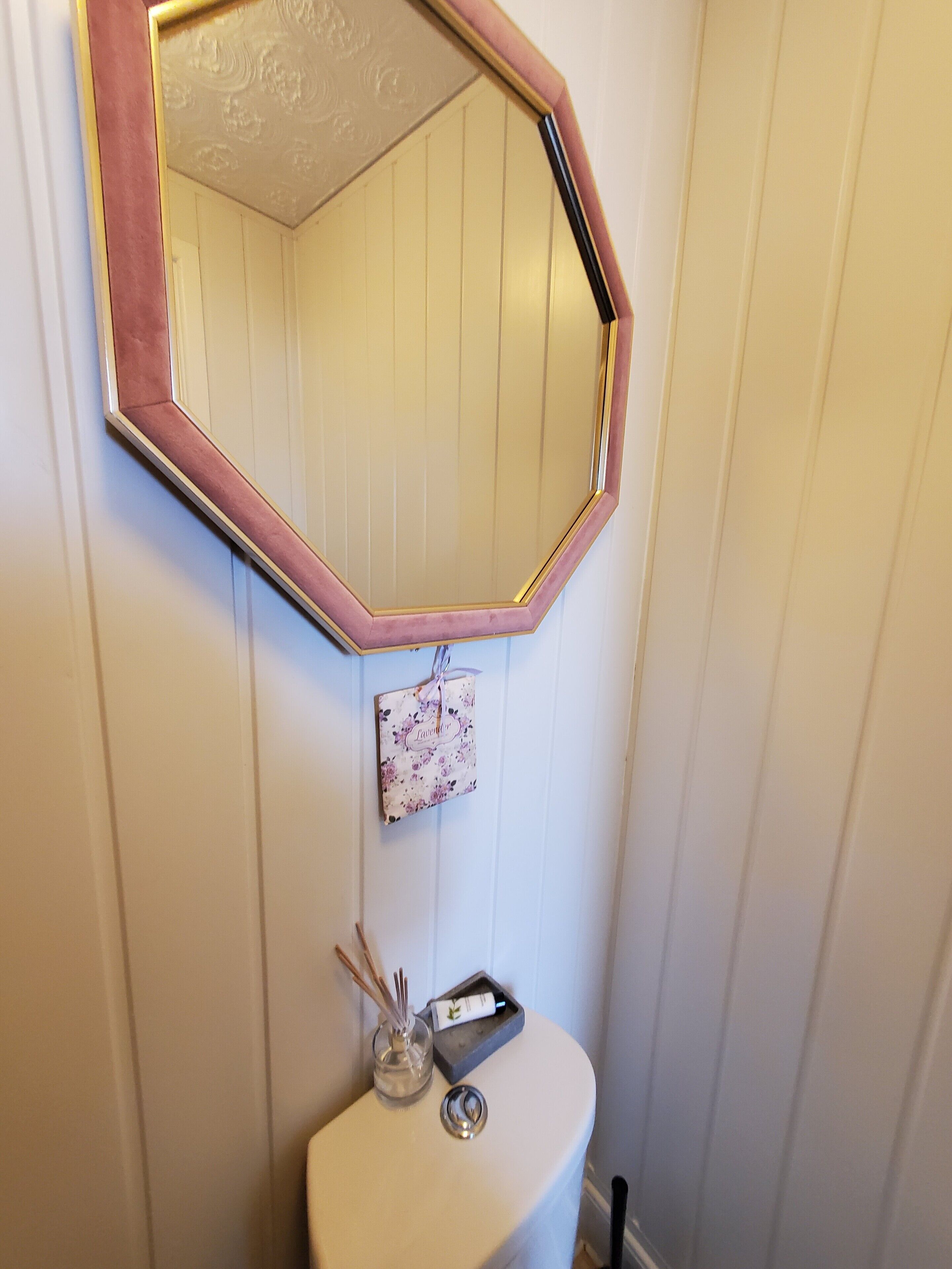Ein Badezimmer mit einer weißen Toilette, einem Spiegel mit rosa Rahmen und einem kleinen dekorativen Gegenstand an der Wand.
