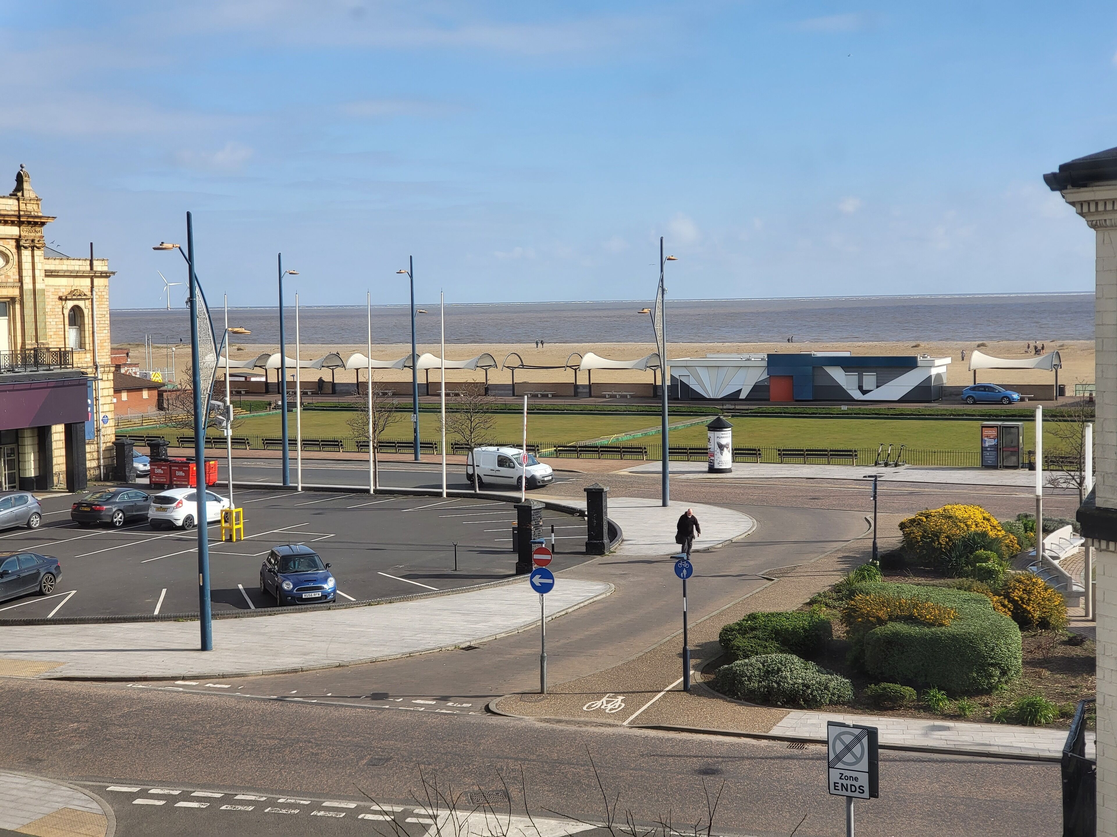 A parking lot with cars, a roundabout, and a beach in the background.