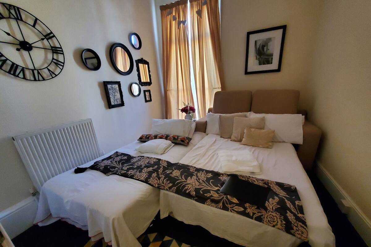 A neatly arranged bedroom with a bed, bedside tables, a radiator, and a clock on the wall.