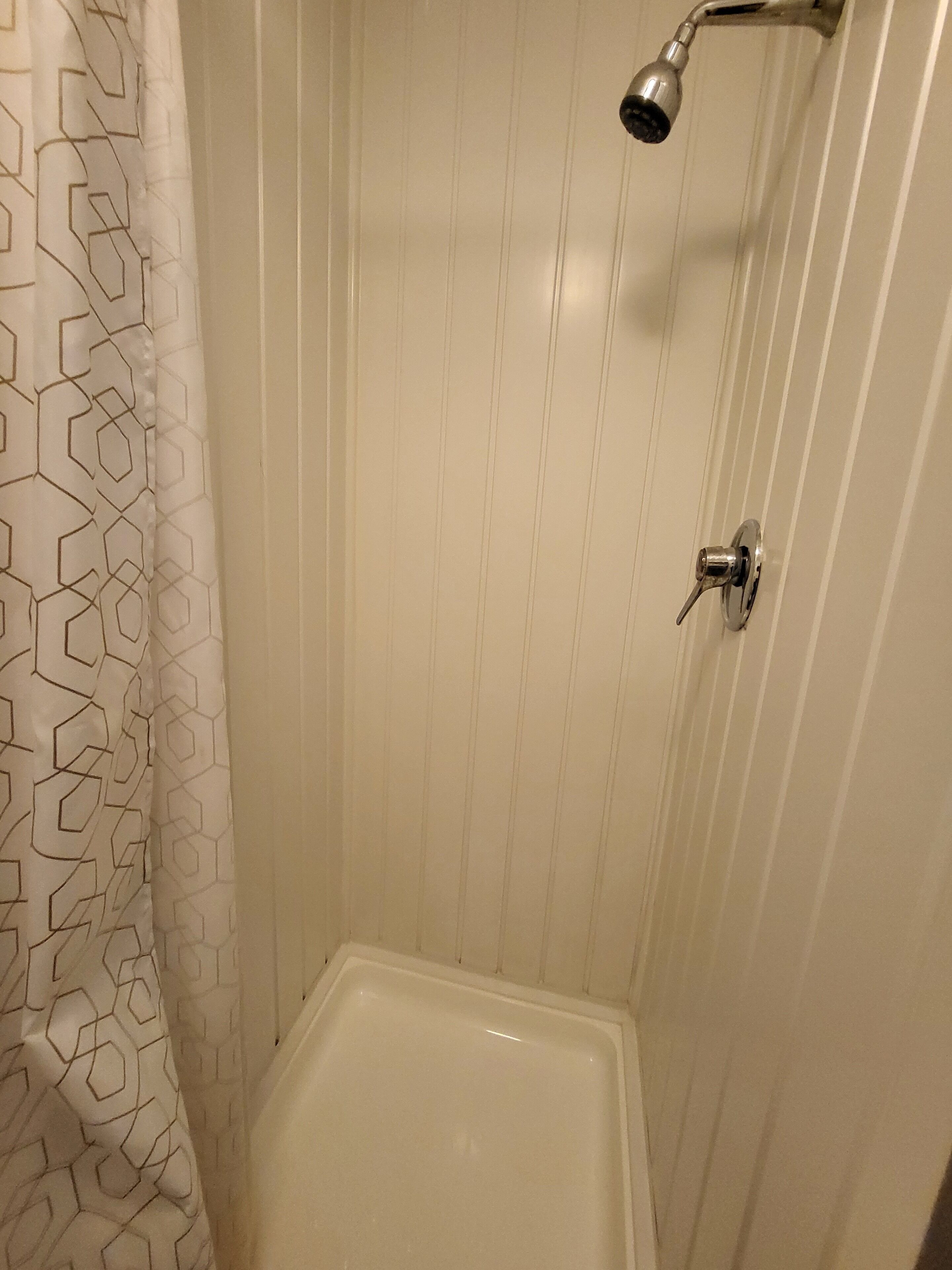 A small, white, tiled shower stall with a showerhead mounted on the wall.