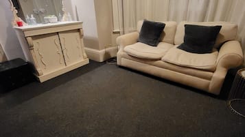 Un salón con un sofá color crema, dos cojines negros, una mesita auxiliar y un espejo decorativo.