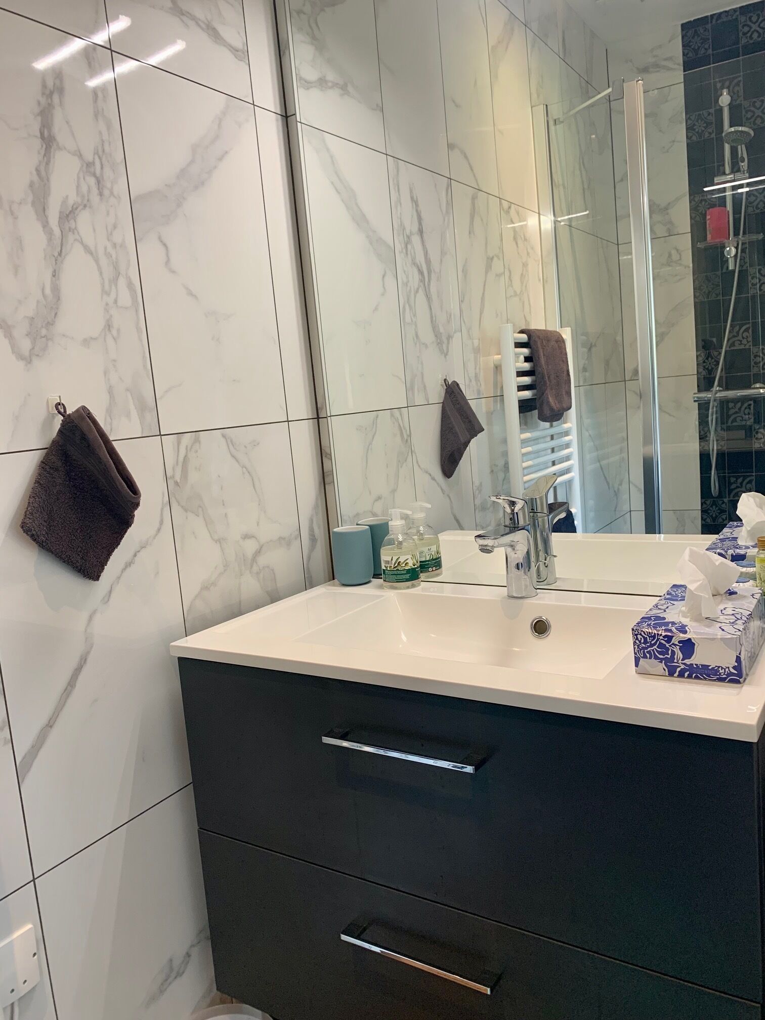 Un baño con pared de azulejos de mármol, un lavabo blanco, un espejo y una cabina de ducha de vidrio.