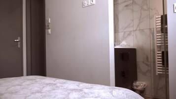 Quarto com cama, uma porta, tomadas e banheiro com chuveiro.