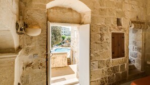 A stone-walled room with a doorway leading to an outdoor swimming pool area. - Dar ta' Lulu - 2 bedroom house with valley views (L-Ghasri)