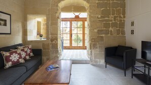 A stone-walled room with a wooden door, a sofa, a coffee table, and a TV. - Dar ta' Lulu - 2 bedroom house with valley views (L-Ghasri)