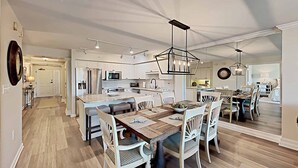 A spacious kitchen with modern appliances, a central island, and a dining area with white chairs and a wooden table. - Sandpiper CRD1C - Beautifully Decorated - Private Stairs to pool and beach (Pawleys Island)