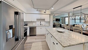 A modern kitchen with white cabinets, stainless steel appliances, and a marble countertop. - Sandpiper CRD1C - Beautifully Decorated - Private Stairs to pool and beach (Pawleys Island)