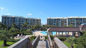 A hotel with multiple balconies, a swimming pool, and a wooden deck leading to the pool area. - Sandpiper CRD1C - Beautifully Decorated - Private Stairs to pool and beach (Pawleys Island)