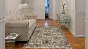 A hallway with a sofa, a patterned rug, a clear glass table, a lamp, and a vase with a plant. - 1900 Athenian House (Athens)