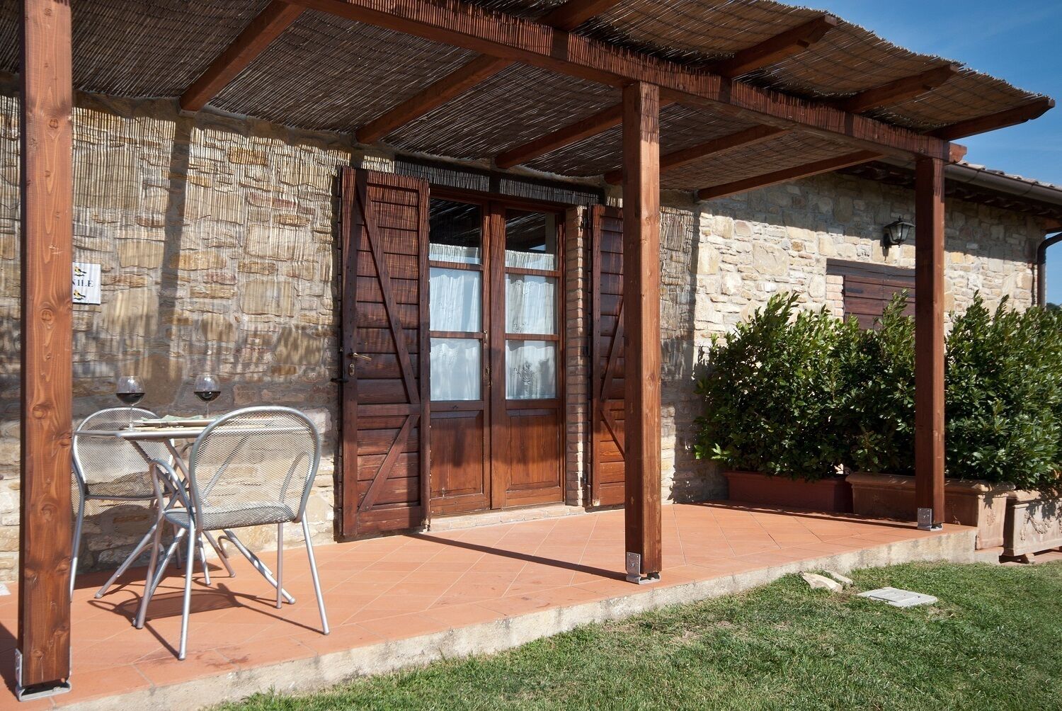 Un espace extérieur aménagé dans un style rustique, avec un mur en pierre, une pergola en bois et une table entourée de chaises.