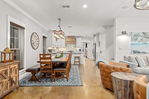A spacious living area with a dining table, chairs, and a sofa. A kitchen is visible in the background.
