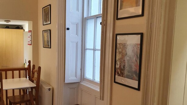 A hallway with a dining table and chairs, a door, and framed artwork on the walls. - Impeccable 1-bed Apartment in Ilfracombe (Ilfracombe)
