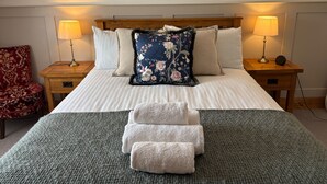 A neatly made bed with white linens, a floral pillow, and two bedside lamps on wooden nightstands. - 1 Keepers Cottage, Skeabost Bridge, Isle Of Skye (Skeabost)