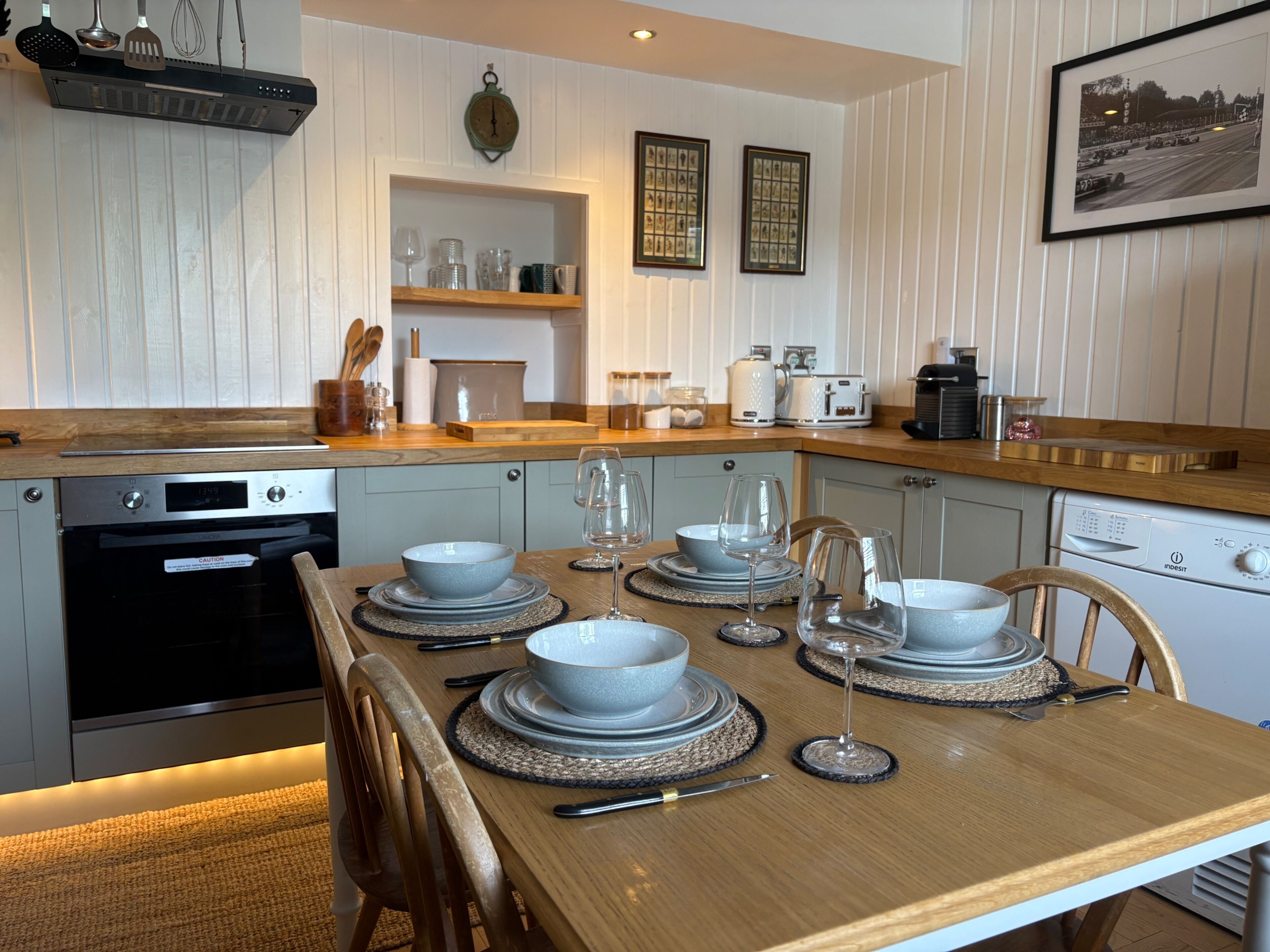 A modern kitchen with a dining table set for four, equipped with a dishwasher, oven, and coffee maker.