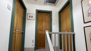 A hallway with wooden doors, a staircase with a white railing, and a framed picture on the wall. - 1 Keepers Cottage, Skeabost Bridge, Isle Of Skye (Skeabost)
