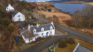A white house with a blue door, surrounded by a rural landscape with a lake and hills. - 1 Keepers Cottage, Skeabost Bridge, Isle Of Skye (Skeabost)