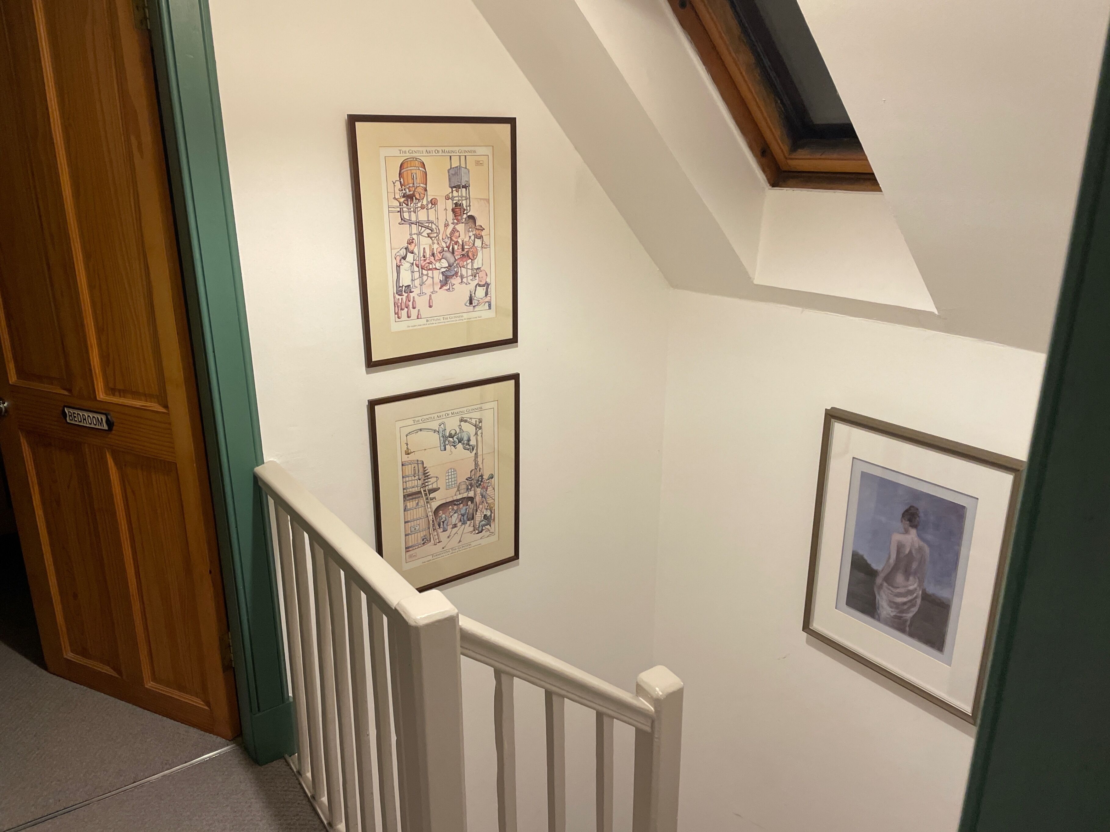 A hallway with framed artwork on the walls, a wooden door labeled "Bedroom," and a white railing.
