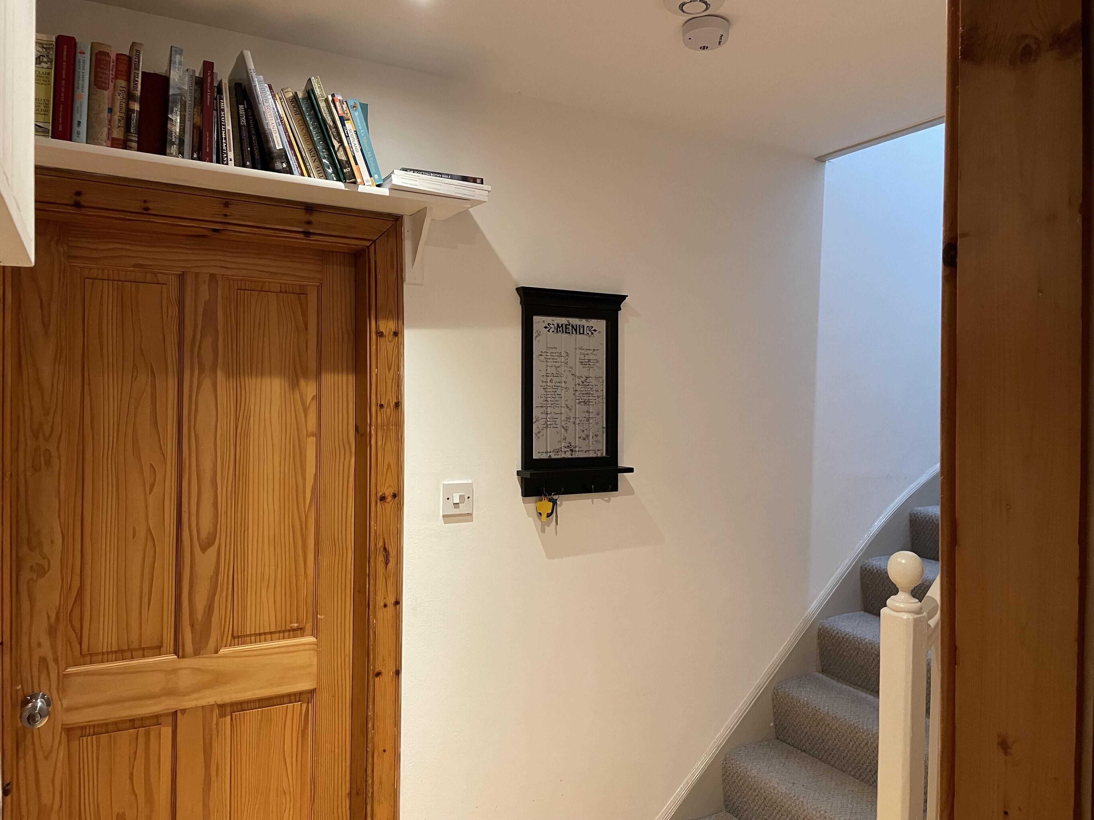 Eine Holztür, ein Bücherregal mit Büchern, eine an der Wand befestigte Speisekarte und eine Treppe.