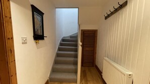 A narrow hallway with a wooden floor, a white radiator, and a door leading to a staircase. - 1 Keepers Cottage, Skeabost Bridge, Isle Of Skye (Skeabost)