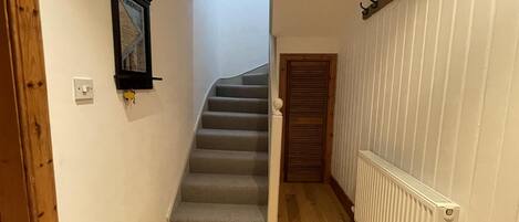 A narrow hallway with a wooden floor, a white radiator, and a door leading to a staircase.