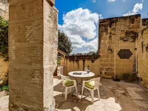 Un patio de piedra con una mesa redonda y dos sillas, una botella y un vaso sobre la mesa.