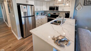 A modern kitchen with white cabinets, stainless steel appliances, and a marble countertop. - Surf Condos 318 - Ocean Views & Poolside Fun! (Surf City)