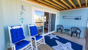 A covered deck with blue cushioned chairs, a starfish-patterned rug, and a wooden ceiling. - Surf Condos 318 - Ocean Views & Poolside Fun! (Surf City)