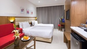 Una habitación de hotel con un sofá rojo, una cama con ropa blanca, una mesita con fruta y un televisor sobre un mueble de madera.