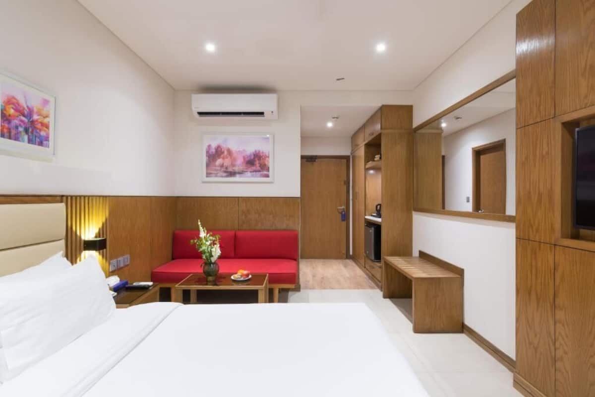 Une chambre d’hôtel avec un lit, un canapé rouge, une petite table avec un vase, des meubles en bois et un téléviseur.