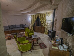 A cozy living room with a sofa, two armchairs, a coffee table, a fireplace, and a TV. - Kalsedon Cave Suites (Nevsehir)