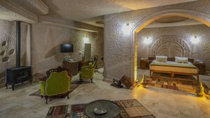 A room with a stone wall, a fireplace, a bed with a headboard, and a television. - Kalsedon Cave Suites (Nevsehir)
