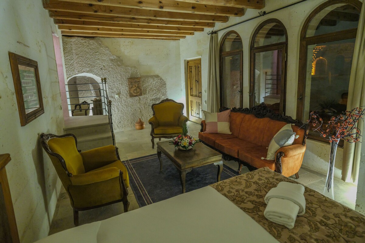 A room with a wooden ceiling, a sofa, a chair, a table, and a window with an arched design.