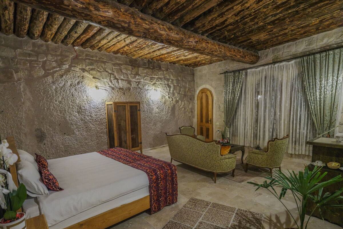 Une chambre avec un lit en bois, un mur en pierre, une armoire en bois, un fauteuil vert, une petite table et une plante en pot.