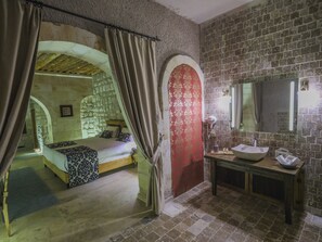 A bedroom with a stone wall, a wooden bed, and a red door. - Kalsedon Cave Suites (Nevsehir)
