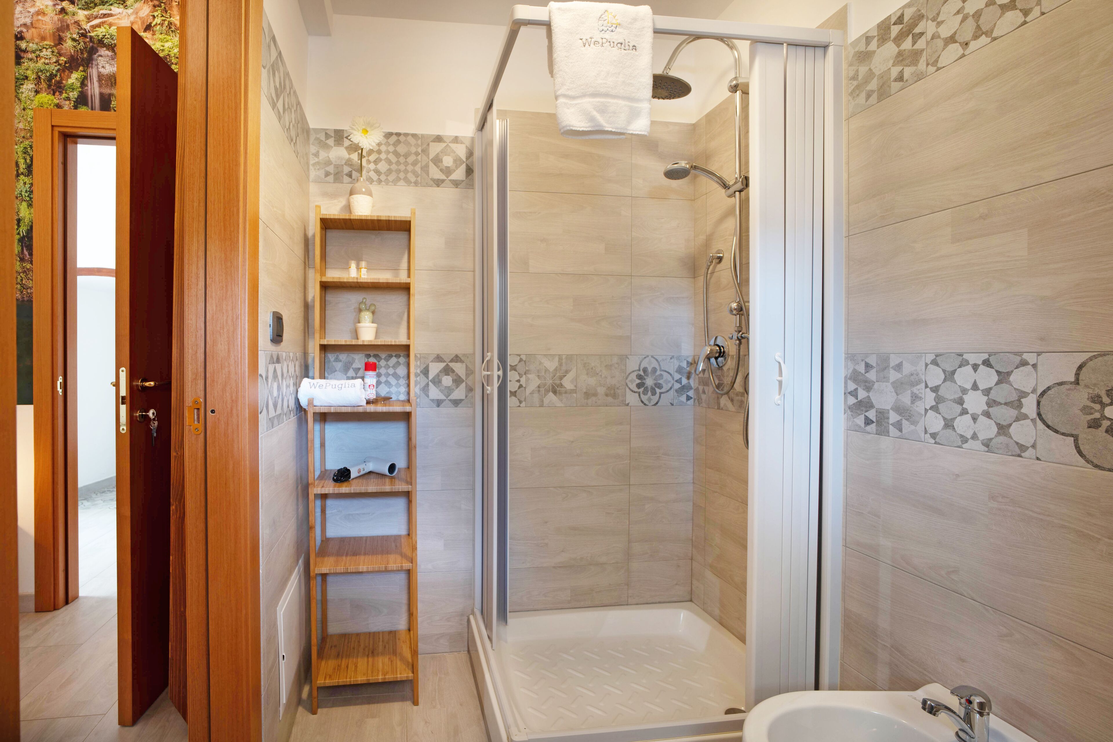 A modern bathroom with a shower, a sink, and a wooden shelf unit.