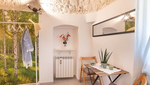 Una habitación acogedora con una silla de madera, una mesita con una planta, un radiador y vistas a árboles a través de una ventana.