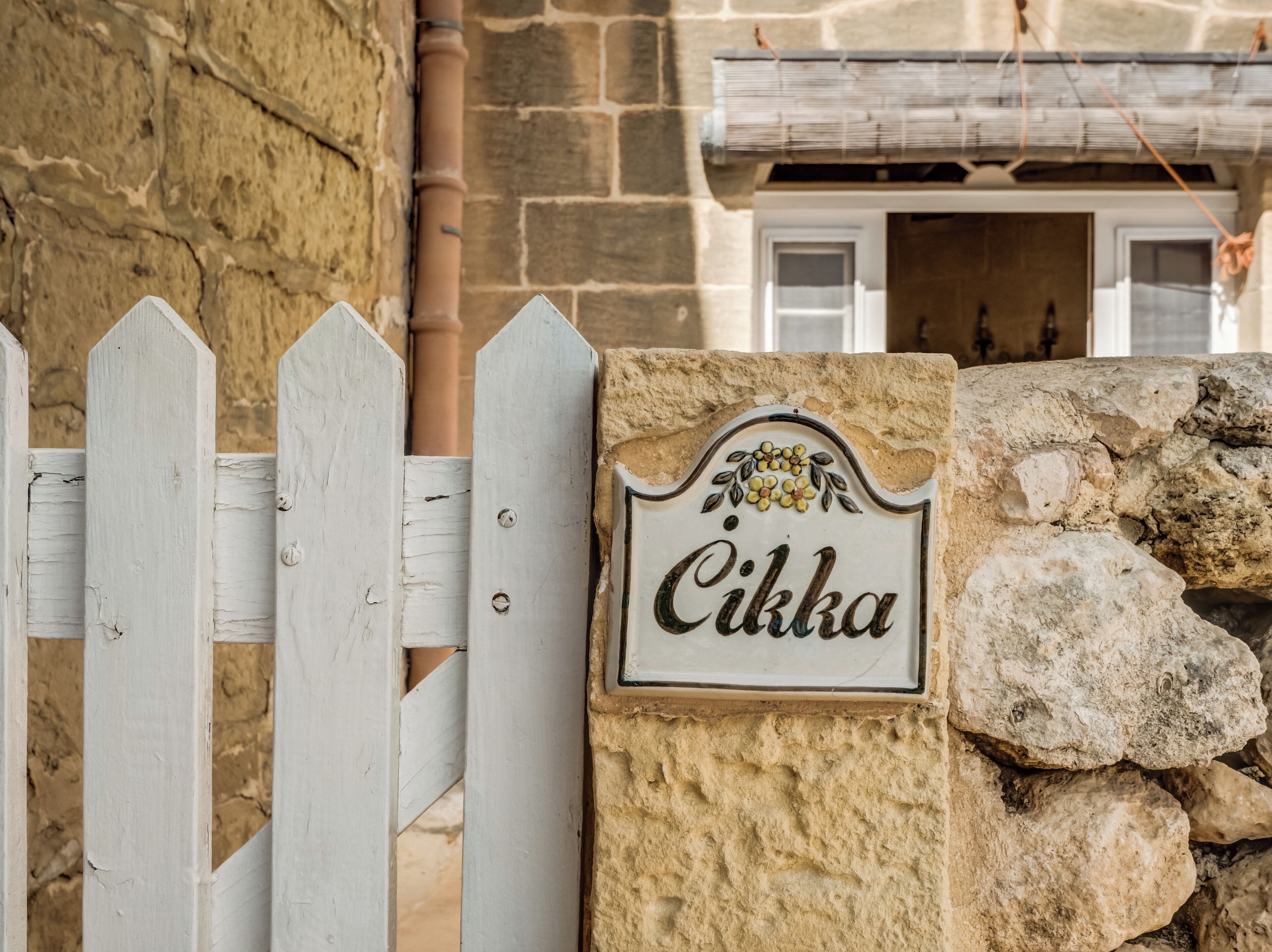 A white picket fence with a stone wall and a sign that reads "Cikka".