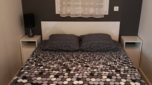 A bed with a black and white polka dot bedspread, two bedside tables, a window with sheer curtains, and a wall switch. - 1 Bedroom Apartment in Fresnes (Fresnes)