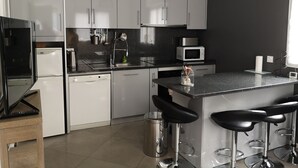 A modern kitchen with white cabinets, a black countertop, a built-in microwave, a dishwasher, and a bar area with stools. - 1 Bedroom Apartment in Fresnes (Fresnes)