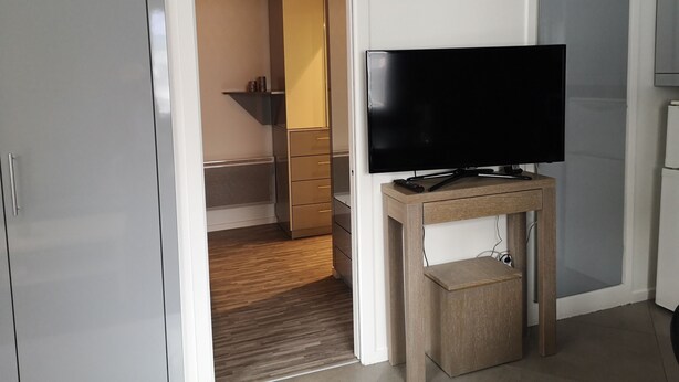 A room with a flat-screen TV on a wooden stand, a wardrobe, and a bathroom visible through an open door. - 1 Bedroom Apartment in Fresnes (Fresnes)