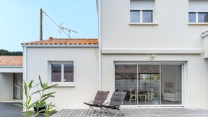 Una casa moderna con patio, due poltrone e una porta scorrevole in vetro che dà su un'area pranzo all'aperto.