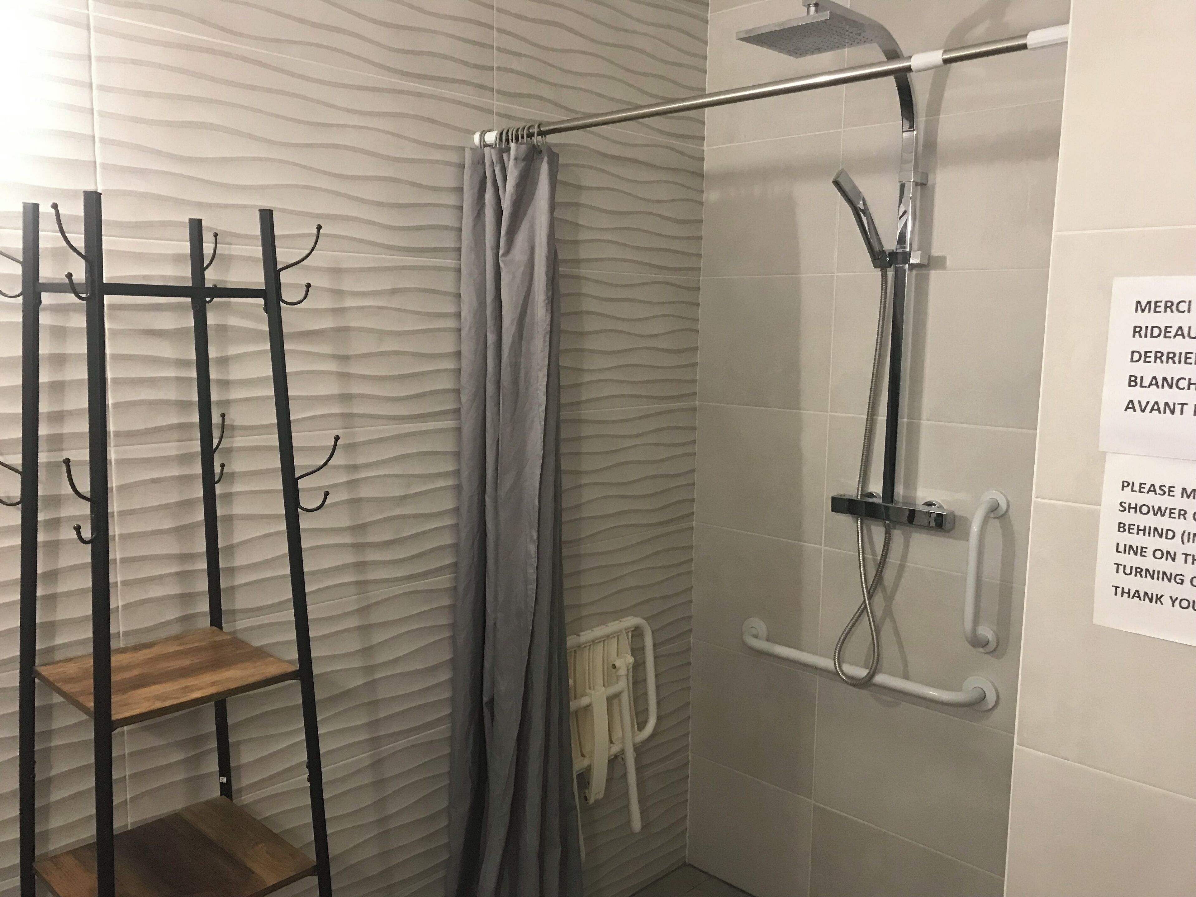 Ein Duschbereich mit Handbrause, Handtuchhalter und einem Holzregal.