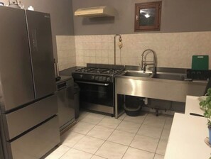 Compact kitchen with modern appliances, featuring a refrigerator, oven, and gas stove, along with a sink and tiled backsplash.