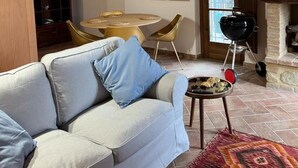 Ein Wohnzimmer mit einer Couch, einem runden Tisch mit Stühlen, einem Grill und gerahmten Pflanzenbildern an der Wand.