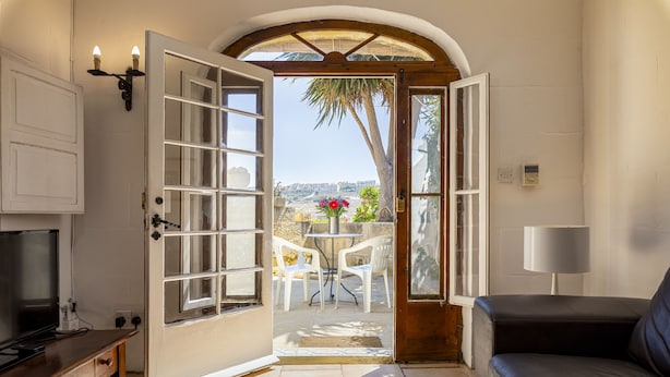 Une porte ouverte donne sur un patio aménagé avec une table et des chaises, un canapé et un téléviseur posé sur un meuble en bois.