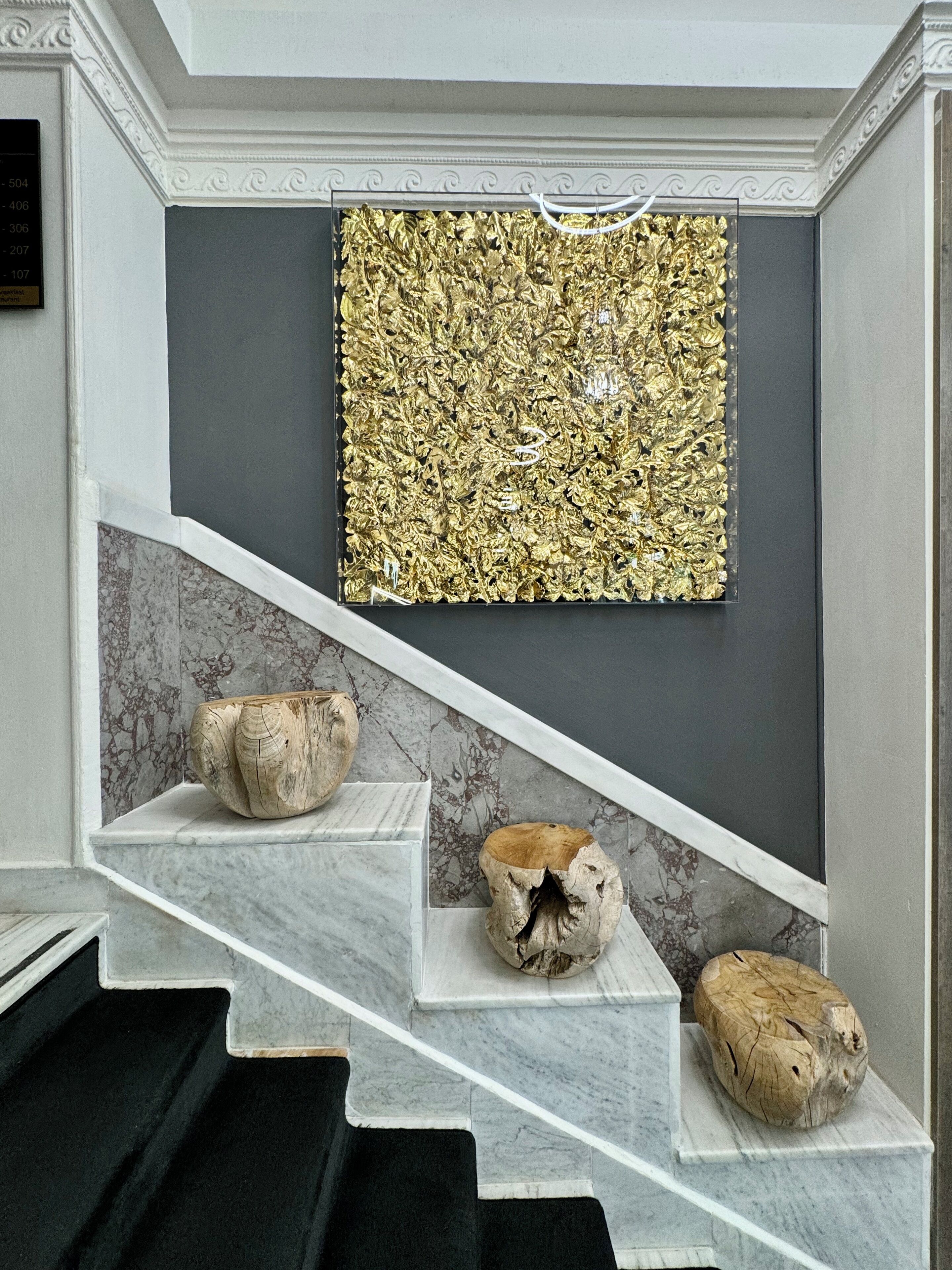 A staircase with three wooden planters on each step, leading to a room with a dark gray wall and a large gold leaf artwork above.