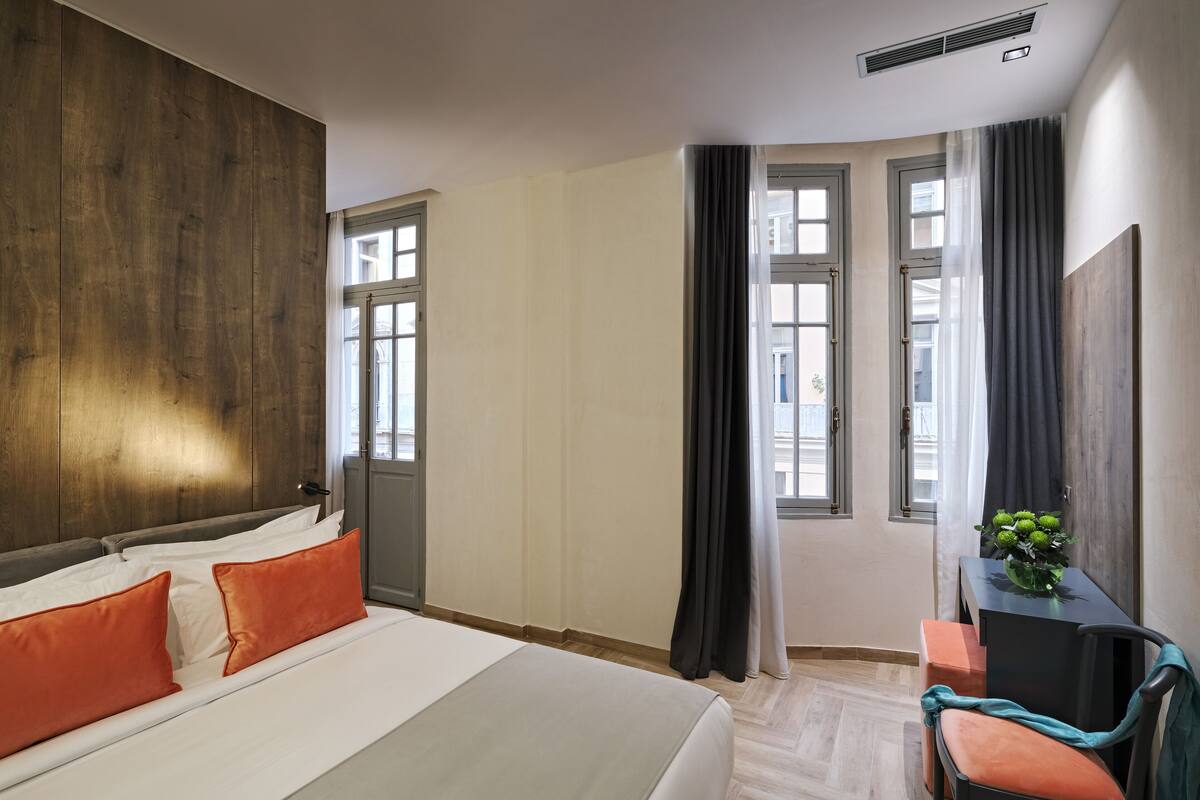 A hotel room with a large bed, a desk with a chair, and a window with curtains.