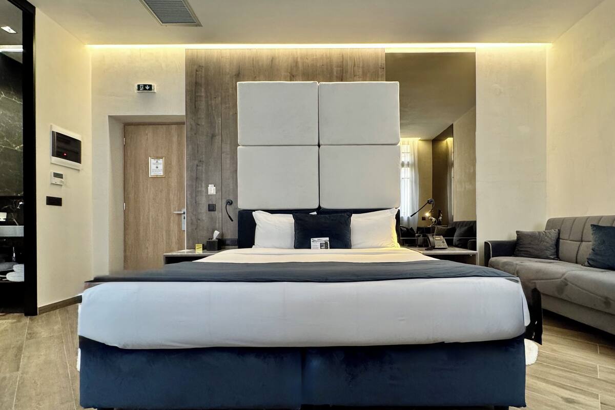 A modern hotel room with a large bed, a sofa, and a desk with a lamp.